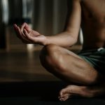 A shirtless man in a yoga studio meditating in the lotus position for relaxation and wellness.