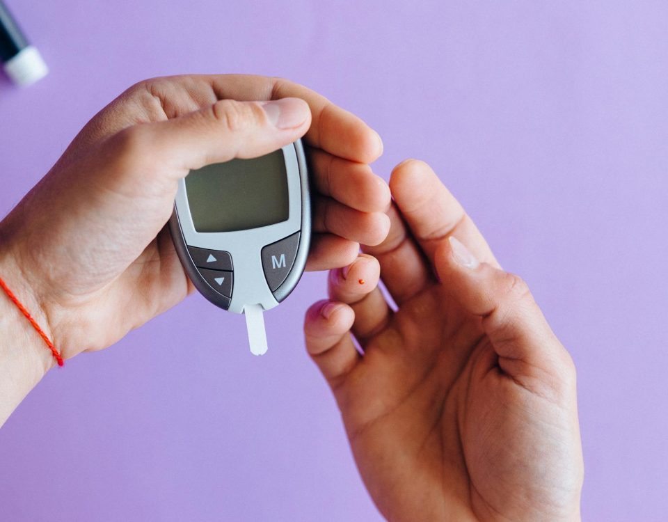 Hands holding a glucometer to test blood sugar levels on a purple background.
