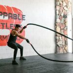 Athletic man training with battle ropes in a gym with motivational wall art.