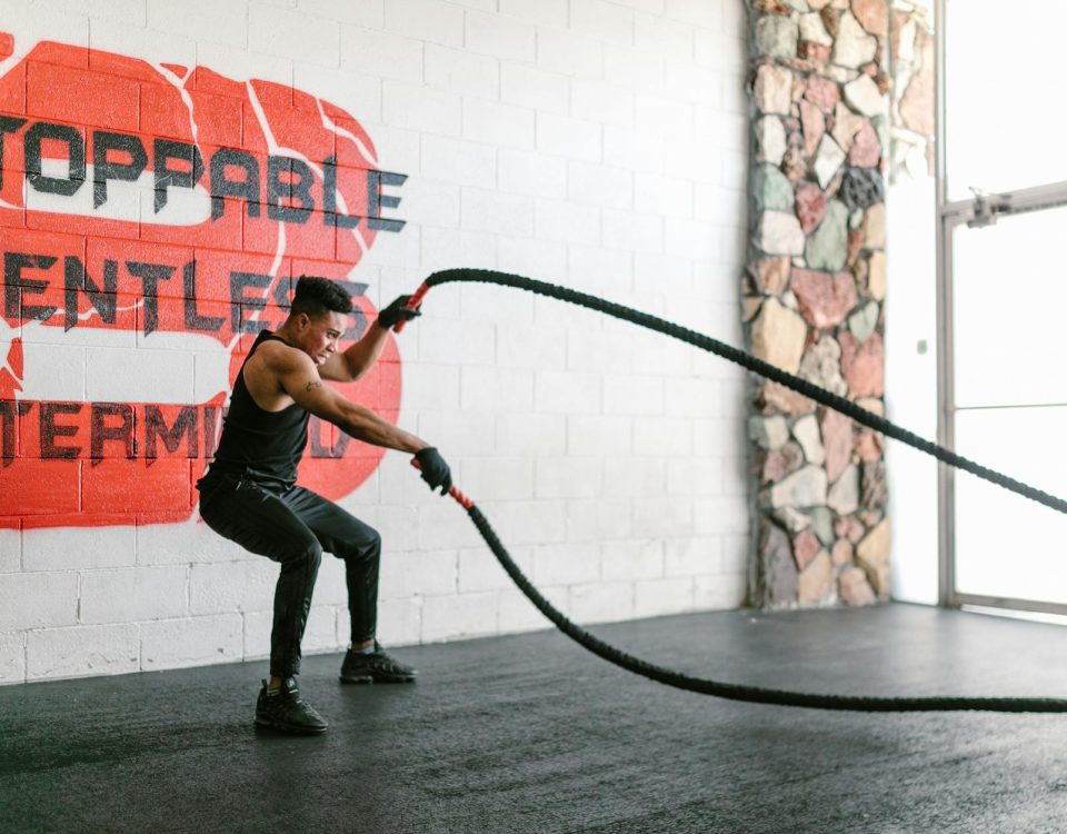 Athletic man training with battle ropes in a gym with motivational wall art.