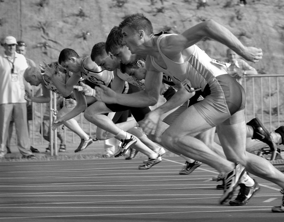 Athletes burst from the blocks during a sprint race, captured in monochrome.