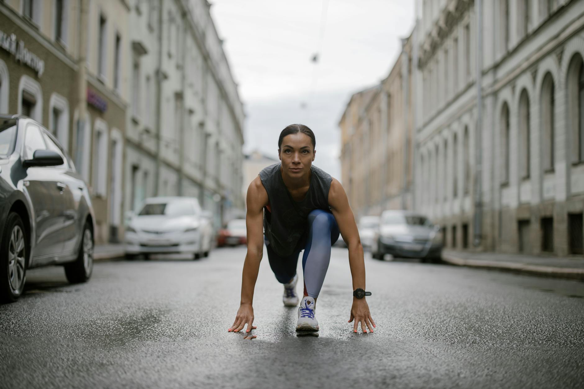 Woman in activewear poised for a run on a city street, symbolizing fitness and determination.