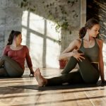 Two women practice yoga indoors, focusing on wellness and flexibility.