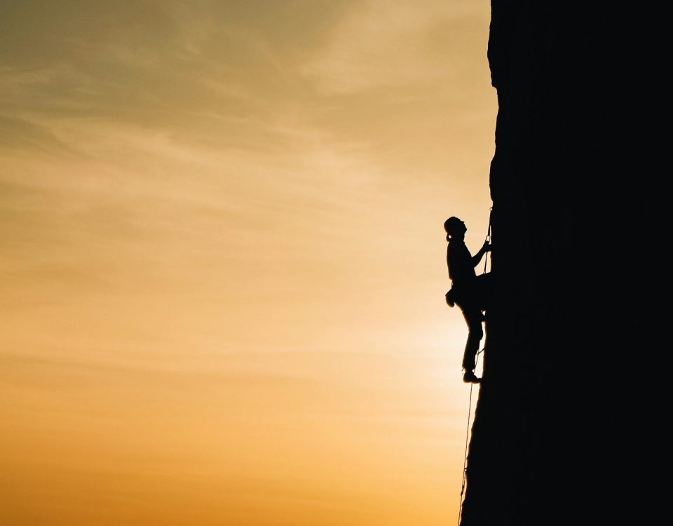 A silhouette of a rock climber scaling a steep cliff during sunset in Russia, showcasing determination and adventure.