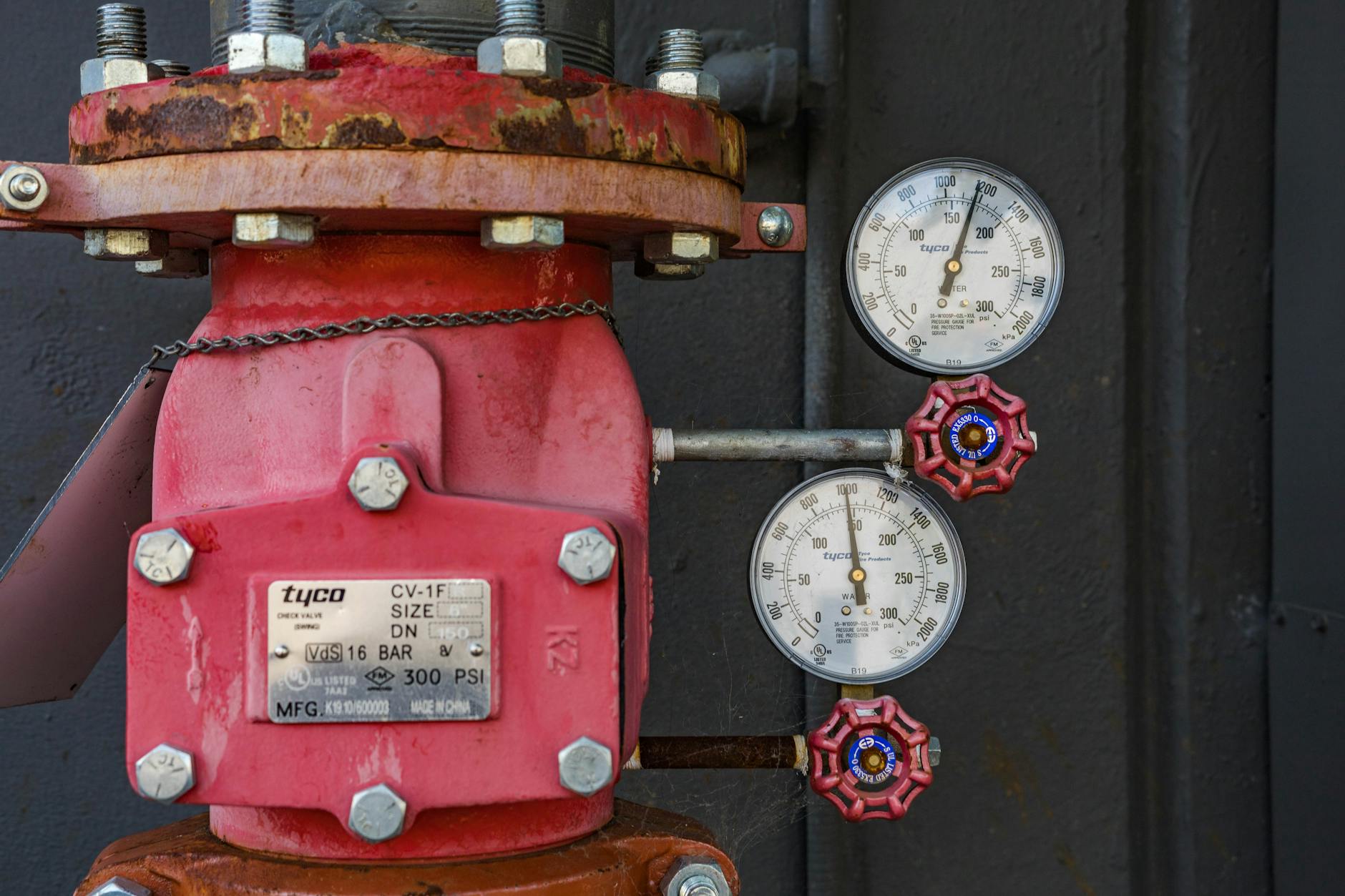 Close-up of industrial pressure gauge and valve mechanism with red paint and rust.