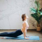 Woman in yoga pose on mat, exercising indoors with natural light and plant decor.