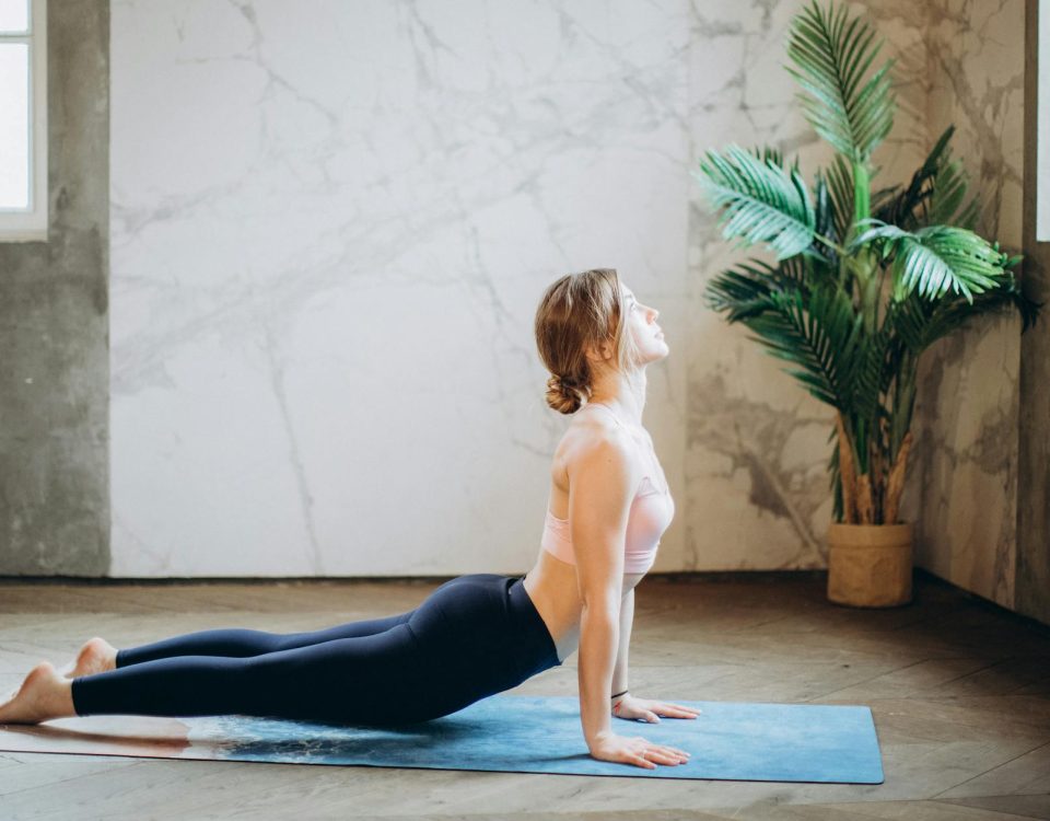 Woman in yoga pose on mat, exercising indoors with natural light and plant decor.