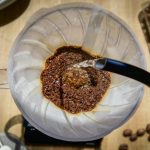 Overhead angle of pour over coffee with fresh grounds and hot water in a glass carafe.