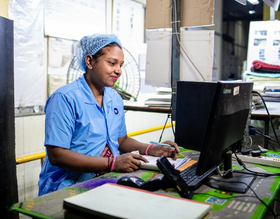 Female factory worker inputs data in a textile manufacturing setting. Indoors and focused.
