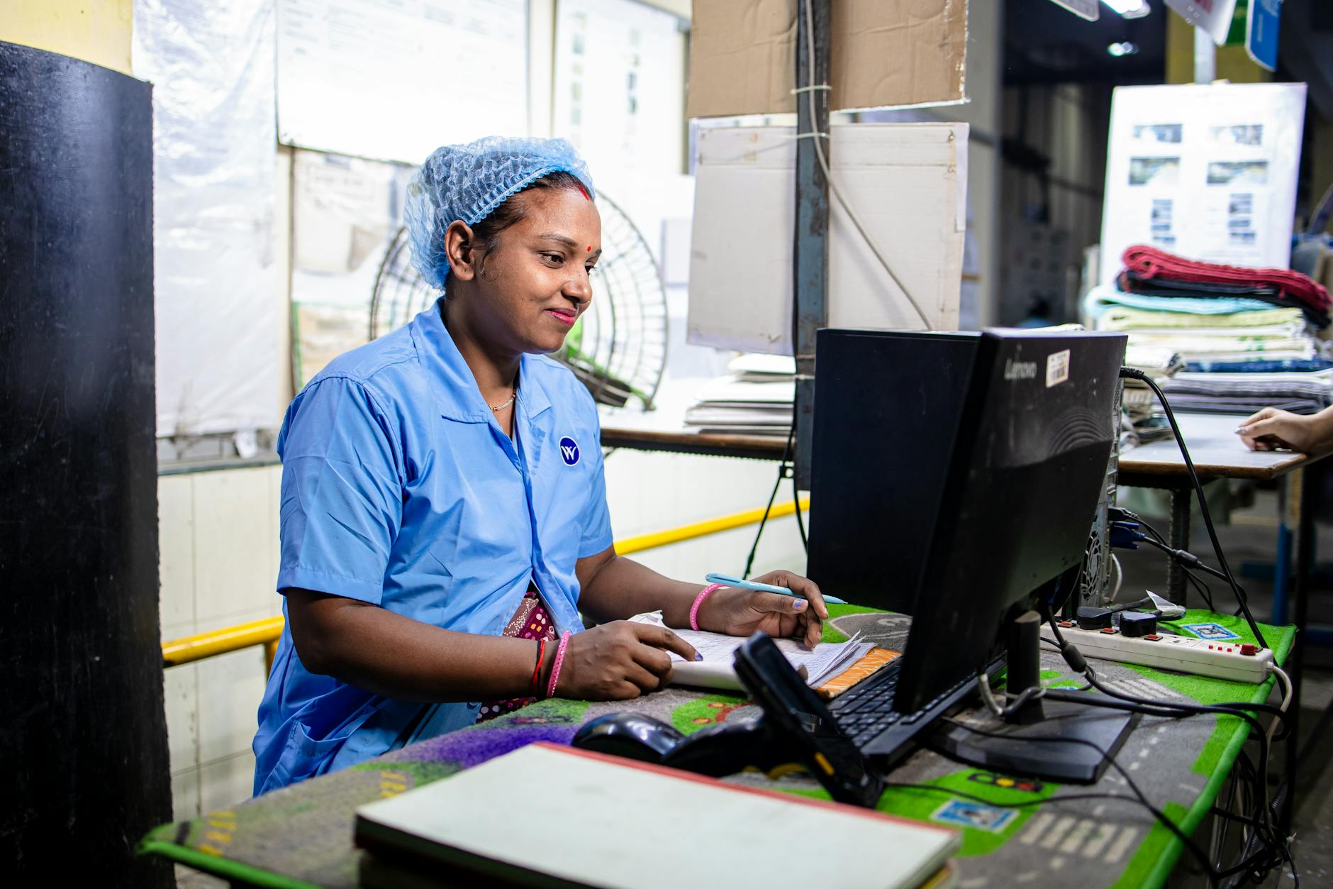 Female factory worker inputs data in a textile manufacturing setting. Indoors and focused.