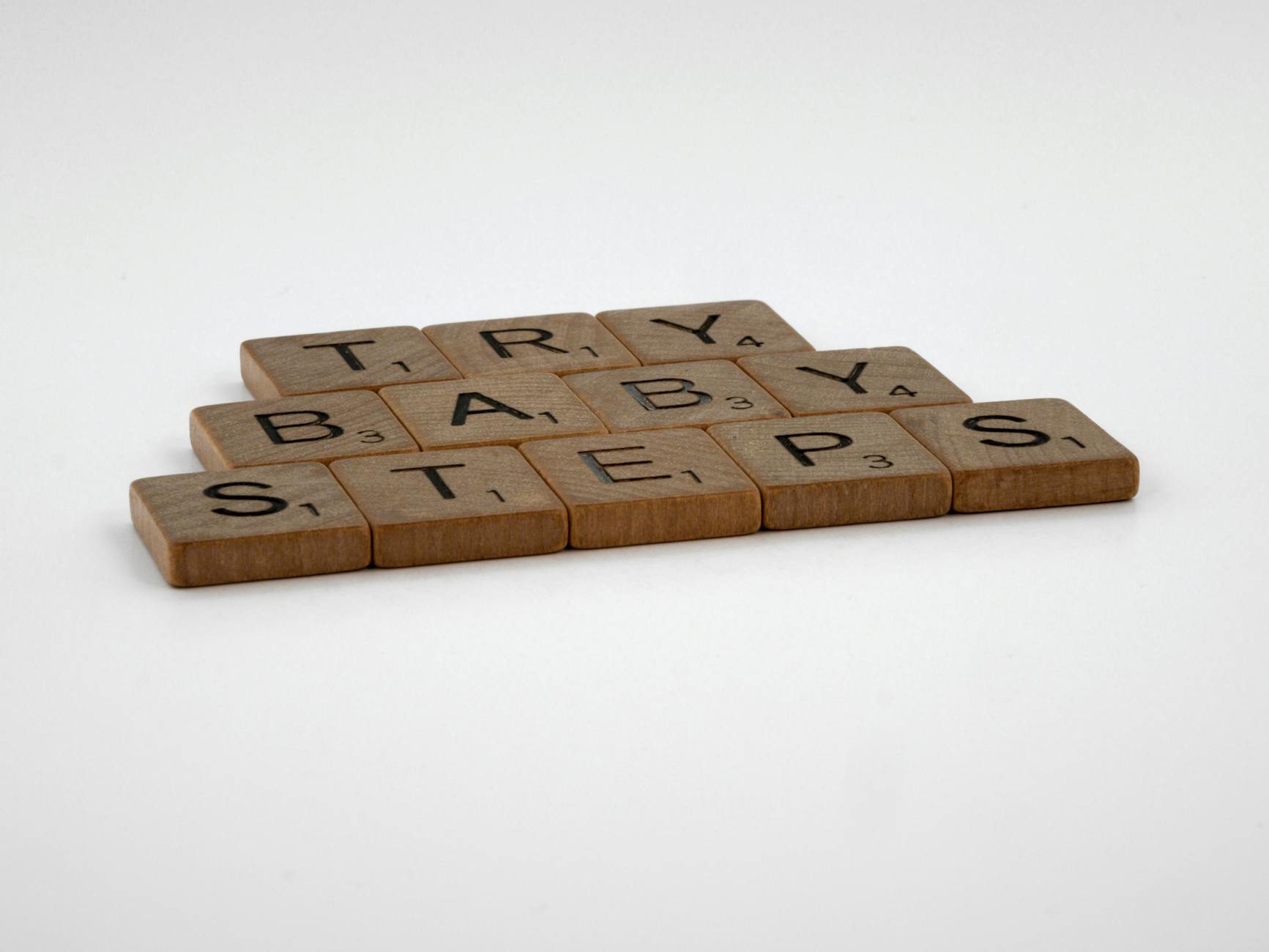 Scrabble tiles forming the phrase 'Try Baby Steps' on a white background.