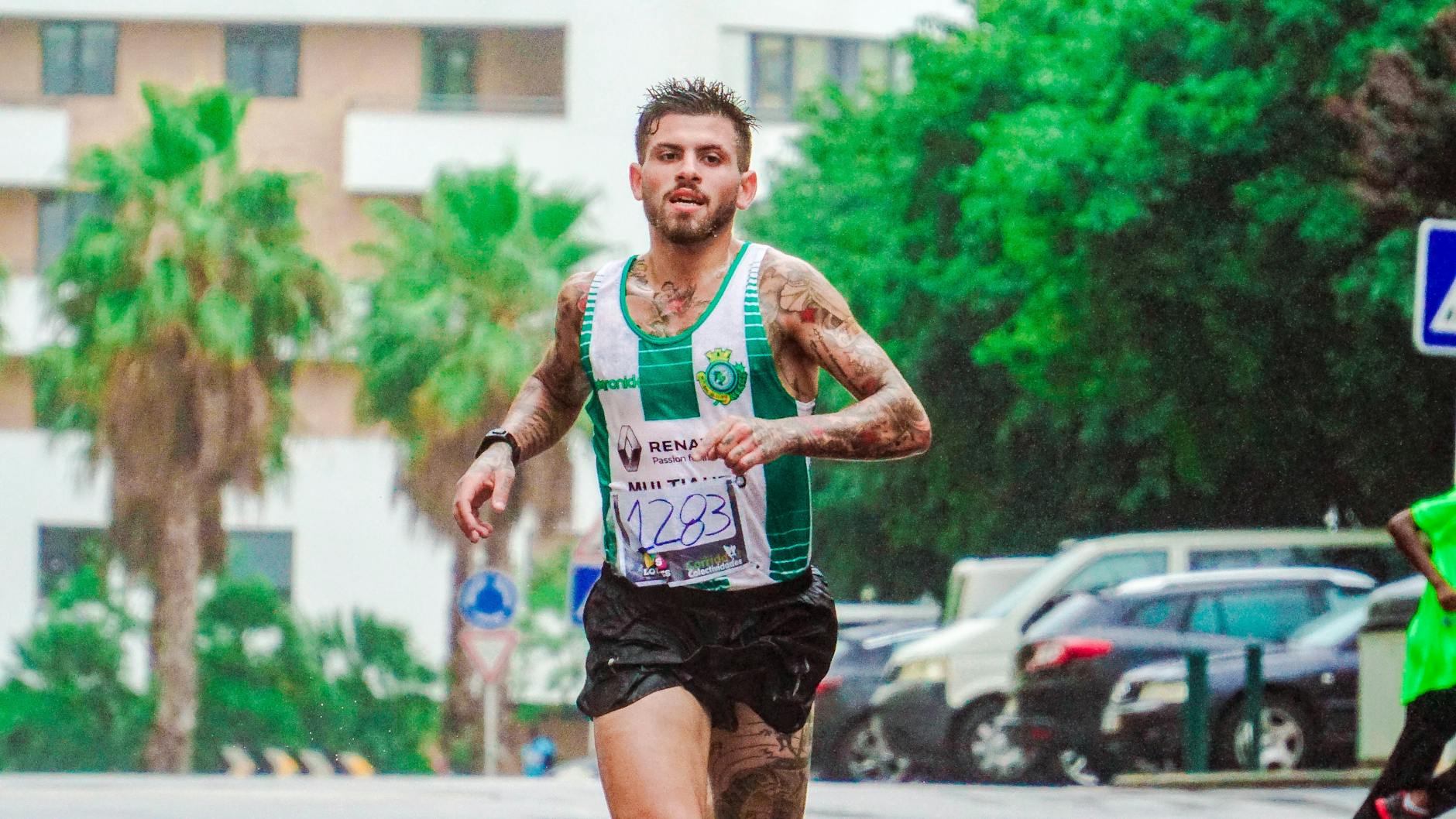 Tattooed male runner participating in a marathon, showing dedication and endurance on a rainy day.