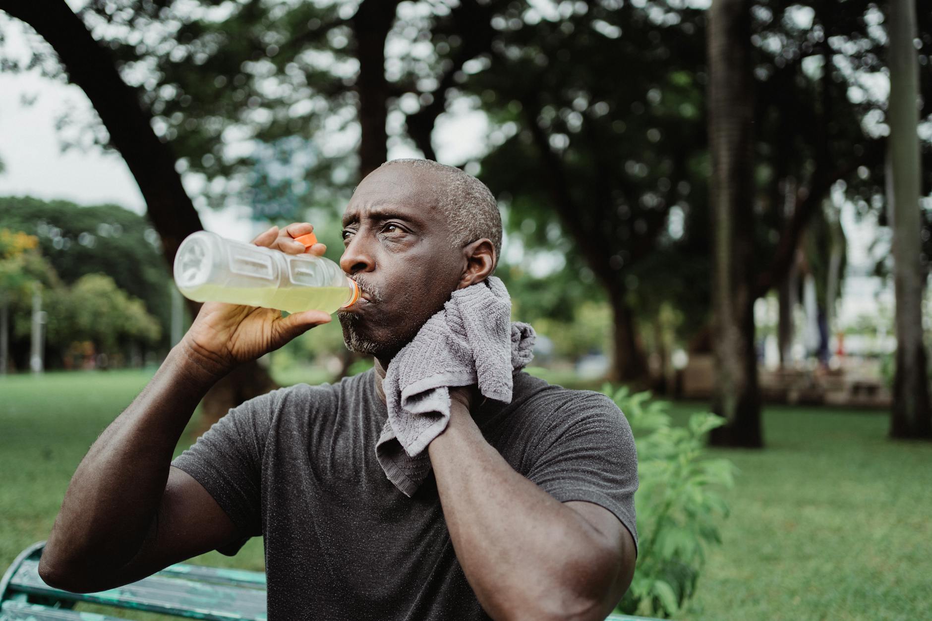 Adult man drinking sports beverage and wiping sweat in a park.