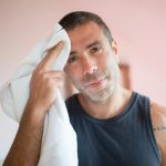A man wipes sweat with a towel indoors, showcasing post-exercise relaxation.