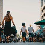 Family walking with stroller and dogs through lively outdoor market street on a sunny day.