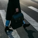 A person crosses a zebra crosswalk holding a stylish black bag in New York City.