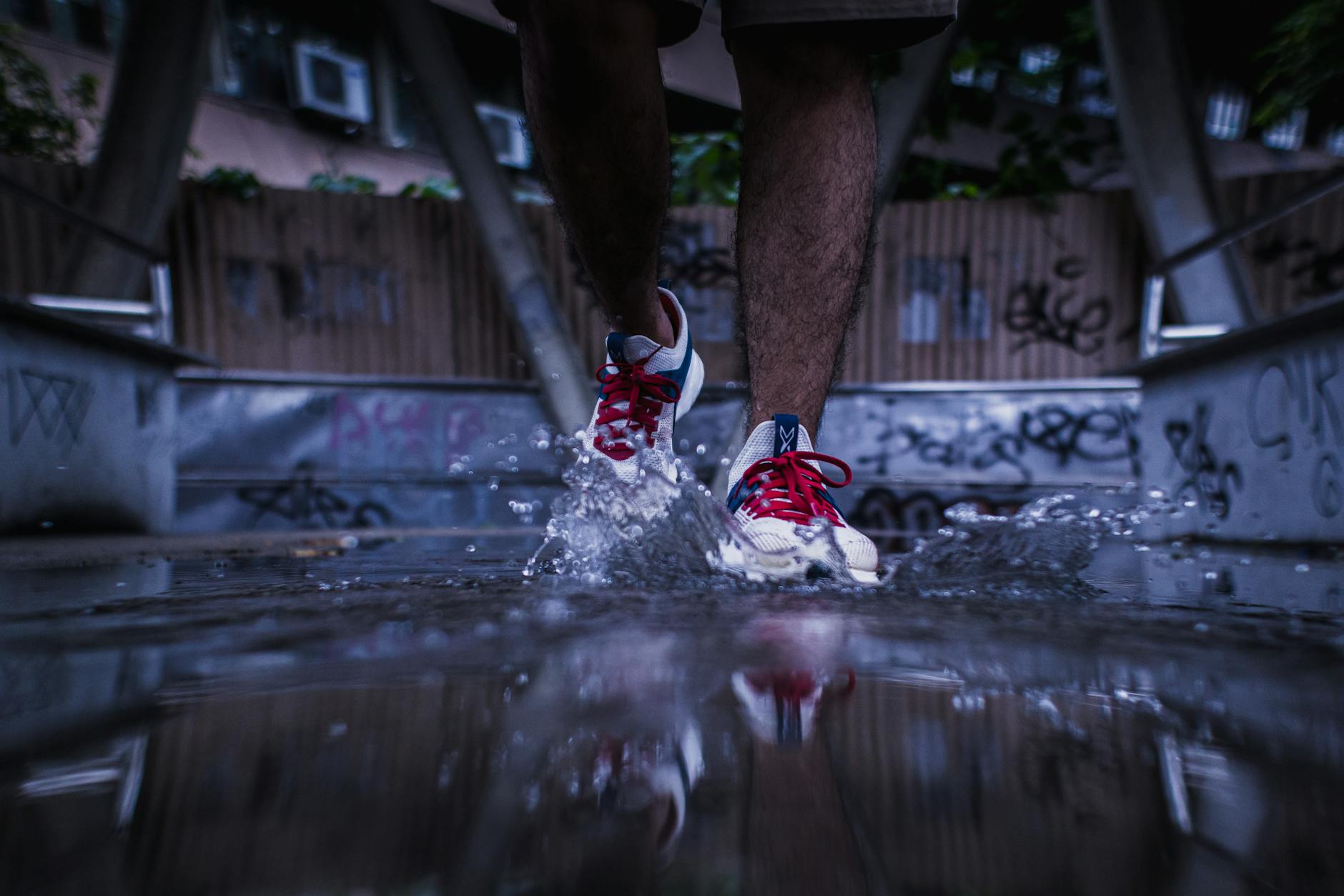 Close-up shot of sneakers splashing through a puddle in a graffiti-covered urban setting.
