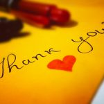Close-up of a thank you note with a heart and pen on colored paper.