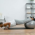 Adult doing push-ups with an exercise ball indoors for fitness and health.